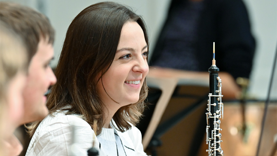 A female student, holding a clarinet, smiling at the camera.